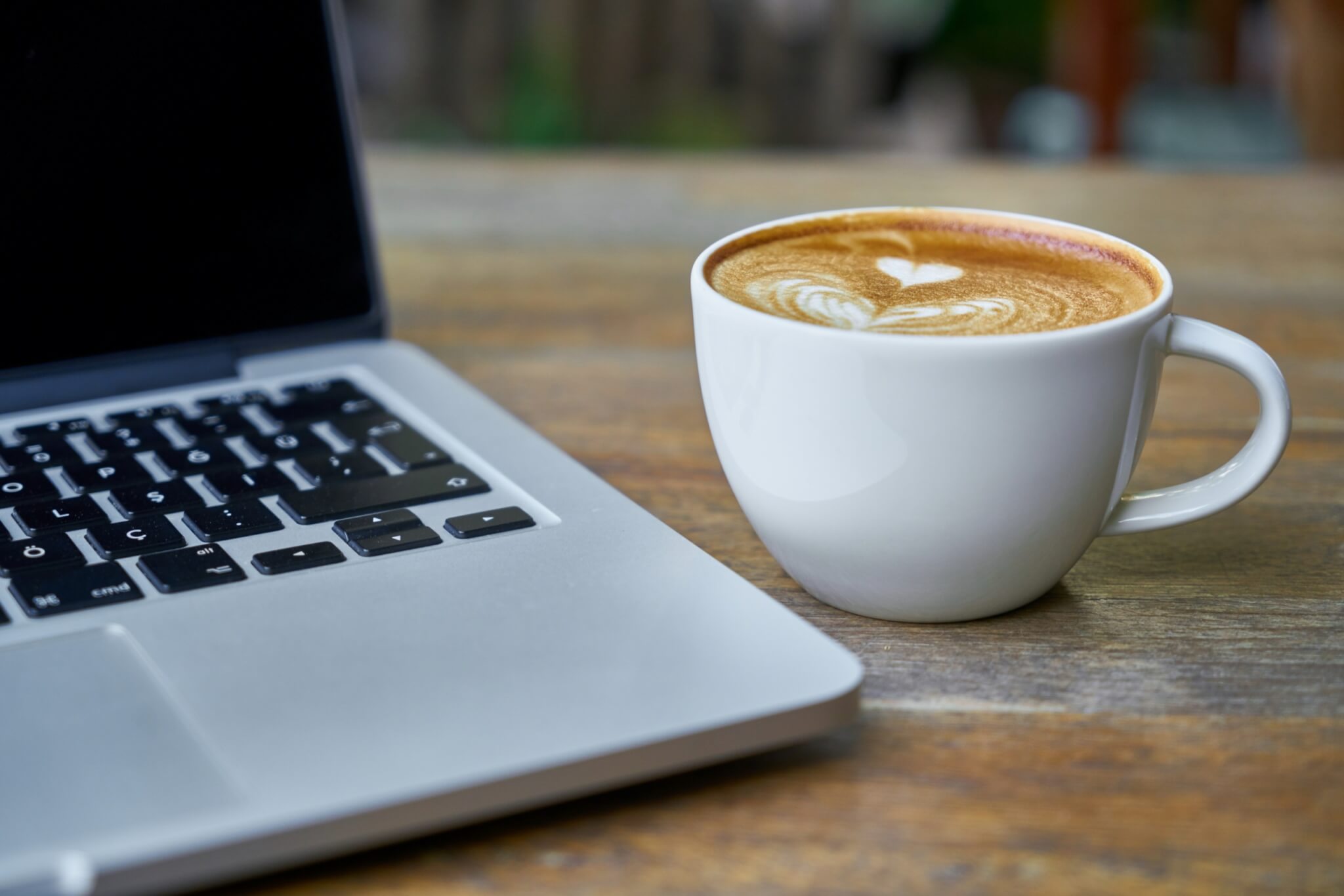 Tasse mit Kaffee und Laptop beim Bindungsfrühstück