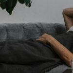 Ein Mann liegt krank auf einer Couch - Sinnbild für den hohen Krankenstand in Deutschland