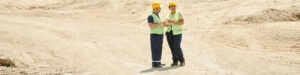 2 Bauarbeiter stehen auf einer Fläche aus Sand und symbolisieren Leistungsbereitschaft
